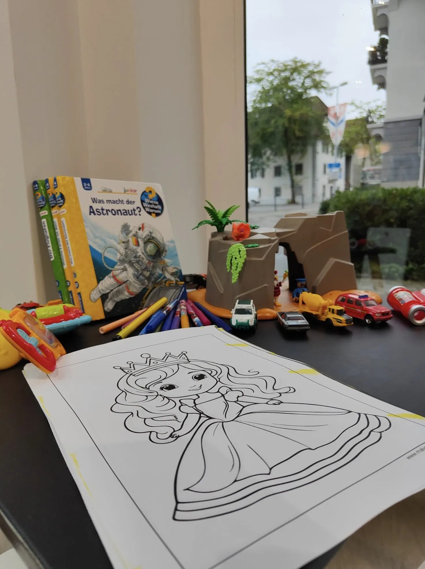 Spielecke der Anklin Apotheke mit Bilderbüchern, Malblatt und Spielsachen am Fenster
