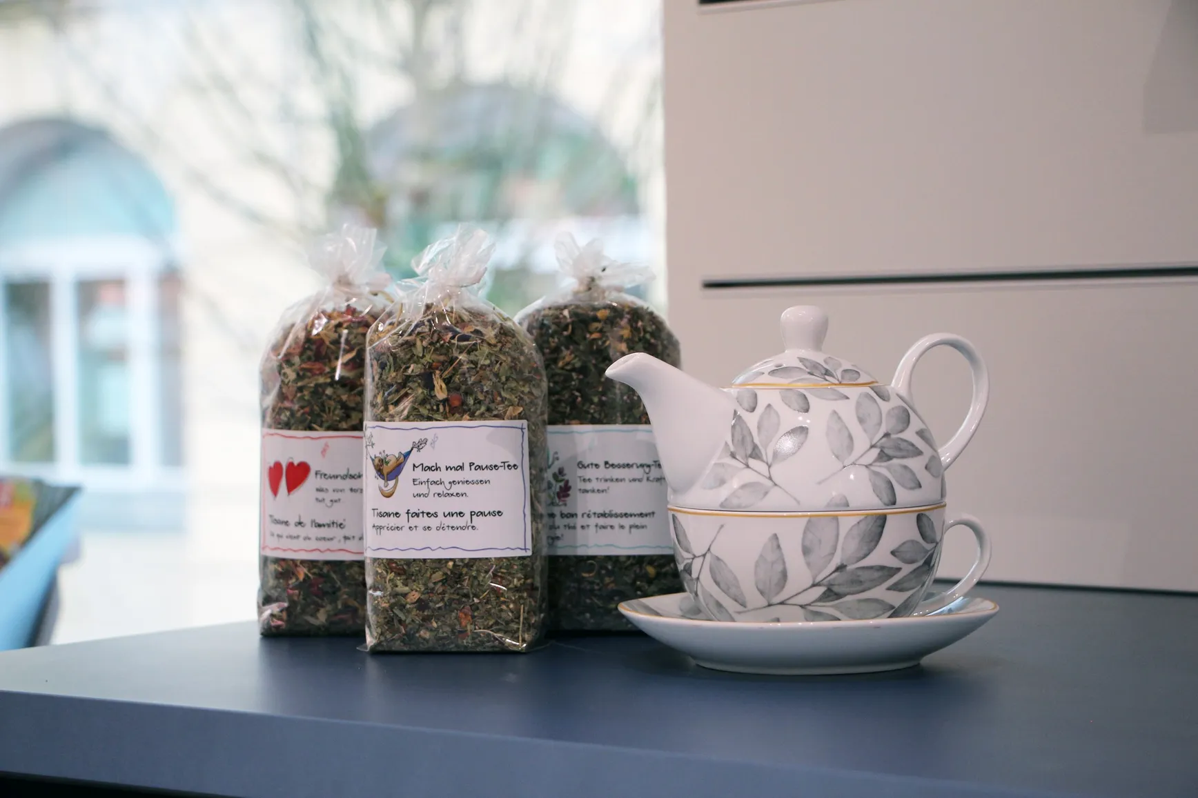 Lose Kräutertees in Beuteln neben einer Teekanne aus Glas